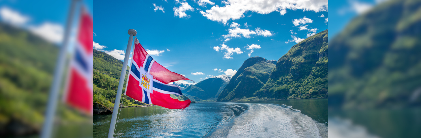 A Norwegian flag waving from the rear of a ship in the Norwegian Fjords.