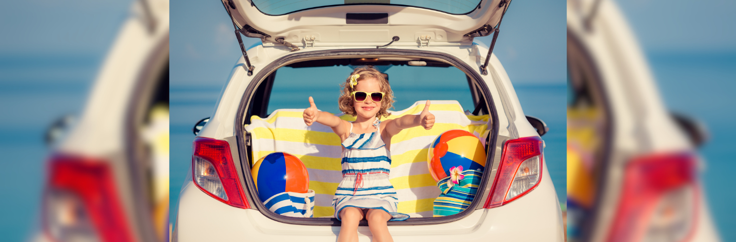 A child on holiday sat in the boot of a car, surrounded by beach gear.