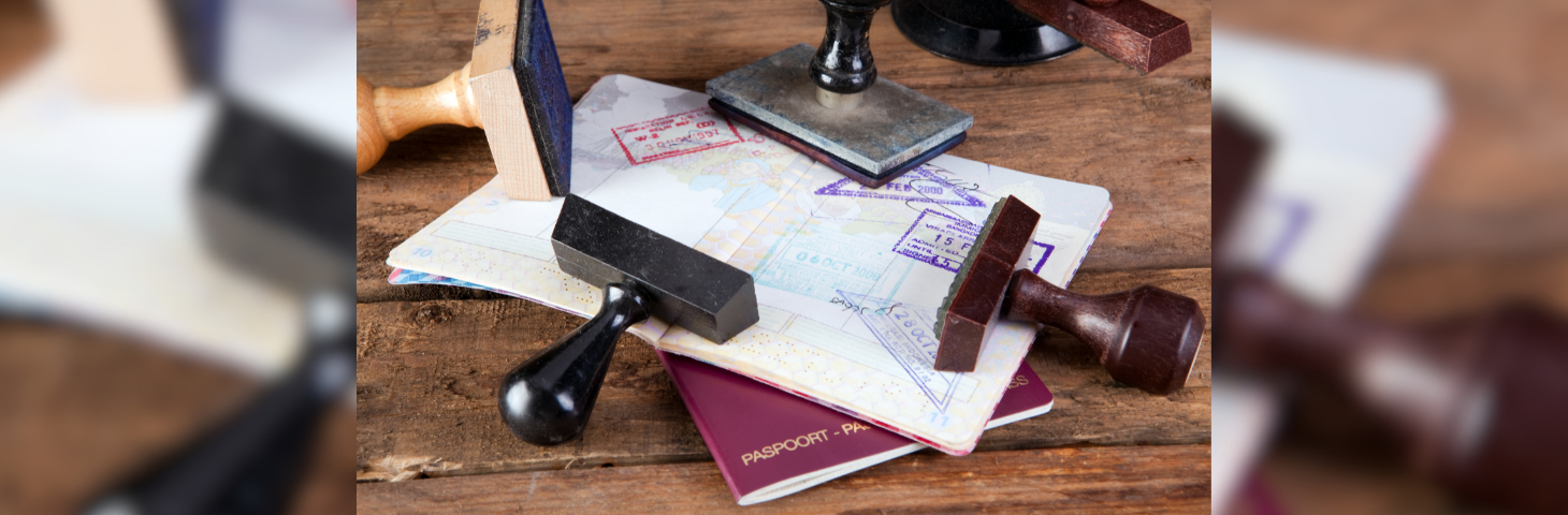 Two passports on a wooden table surrounded by several stamps.