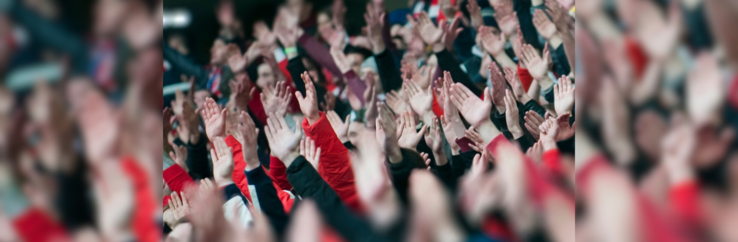 Football fans with their arms raised in a stadium.