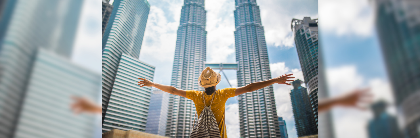 A woman standing in front of the Petronas Towers in Kuala Lumpur, Malaysia with her arms open.