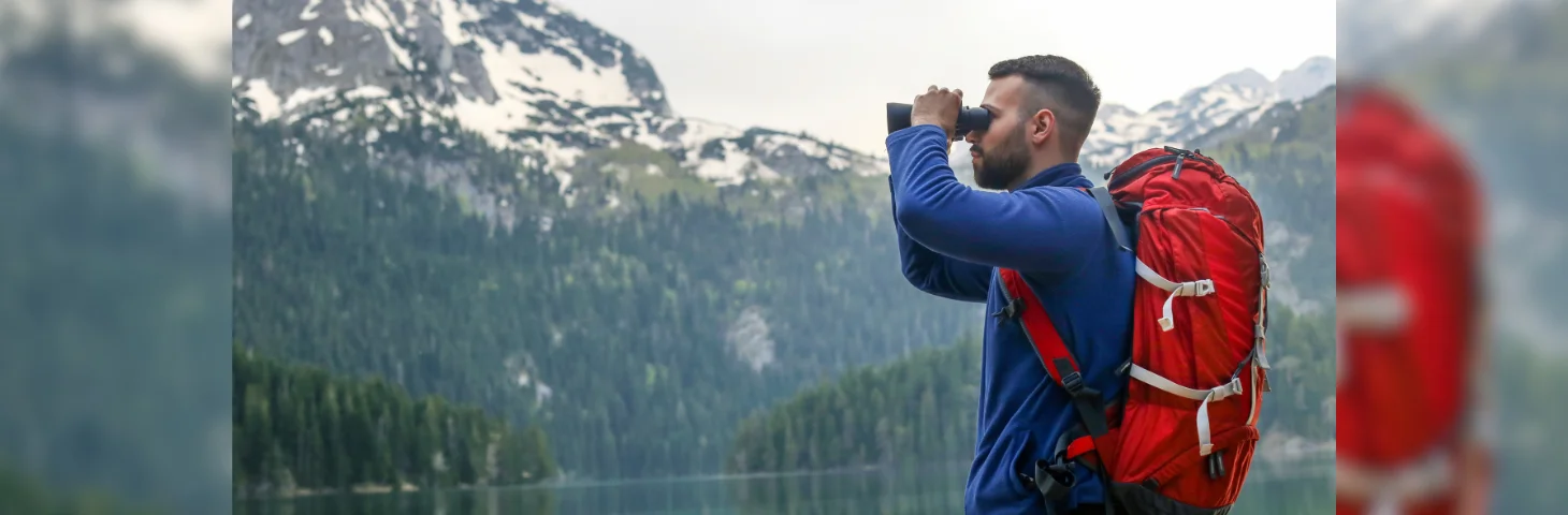 A person on a hike looking through binoculars.