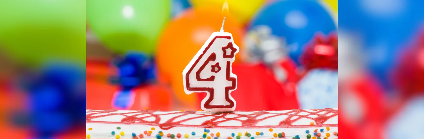 A birthday cake in front of balloons with a '4' candle.