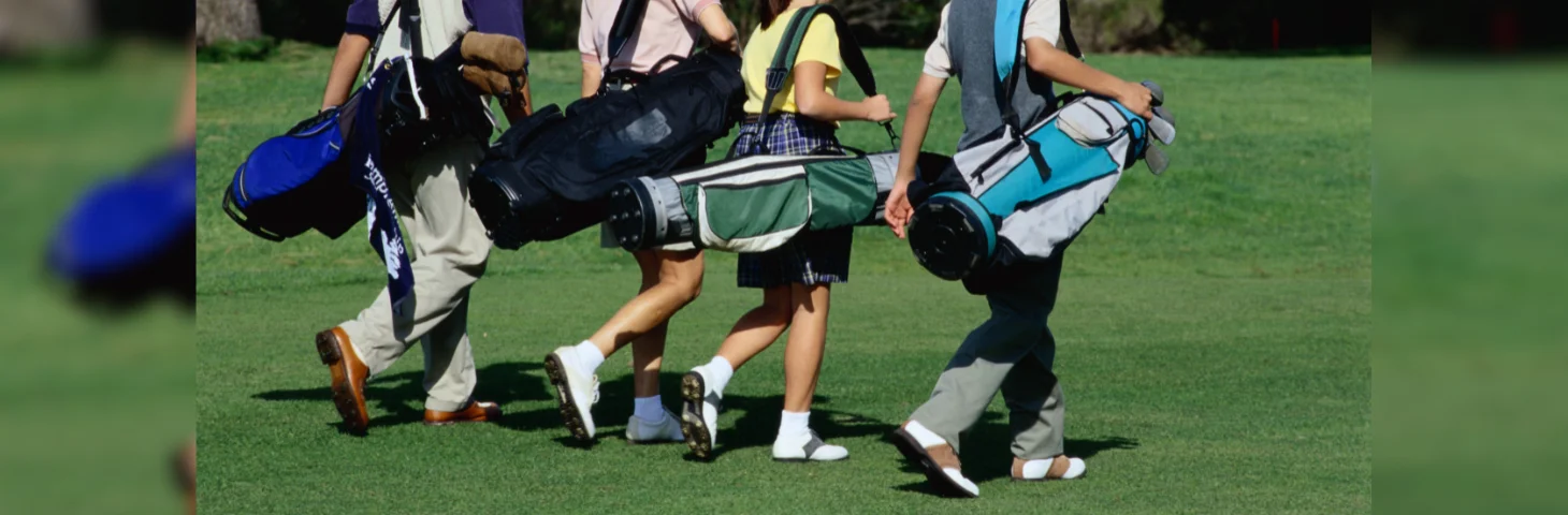 Four golf players carrying their golf bags on the green. 