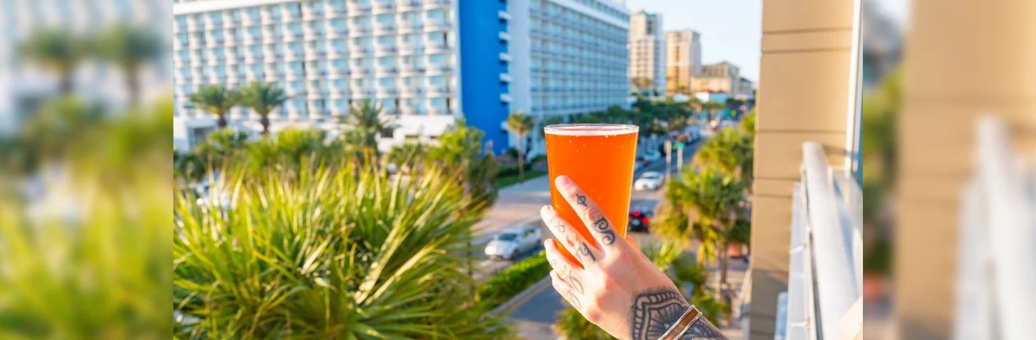 A tattooed person holding a pint glass on the balcony of the 3 Daughters Brewing Co. in Clearwater, Florida.