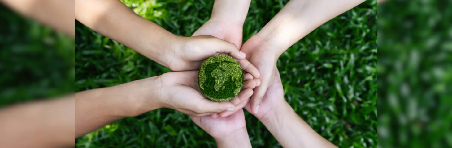 Several hands coming together over a hedge with a green globe in their hands.