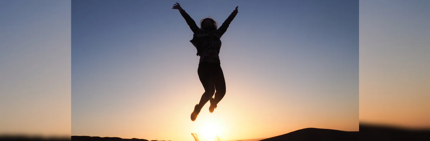 A traveller in the Atlas Mountains at sunset jumping with their hands in the air. 