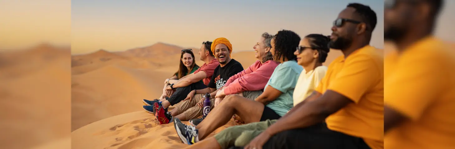 Image of a group of people laughing together on some sand dunes in Morocco