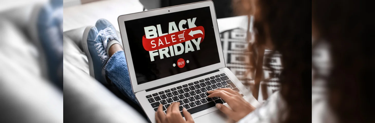 A person with dark hair sat on the couch. Their laptop is open on a screen that says 'Black Friday sale'