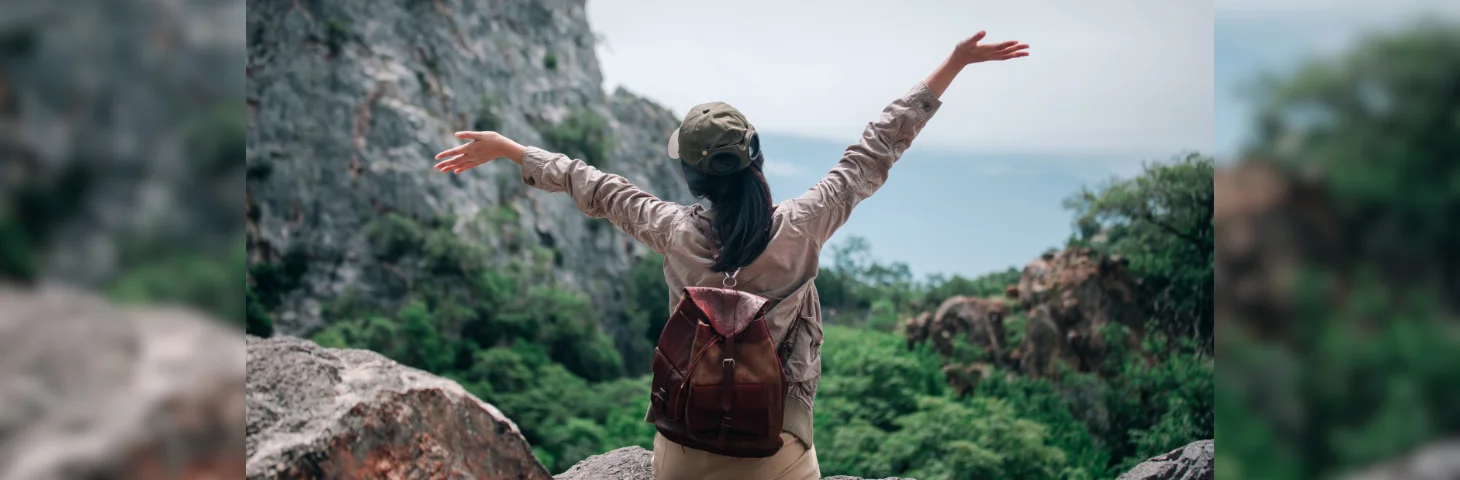 A person with a ponytail and baseball cap on a solo holiday in a mountainous area.