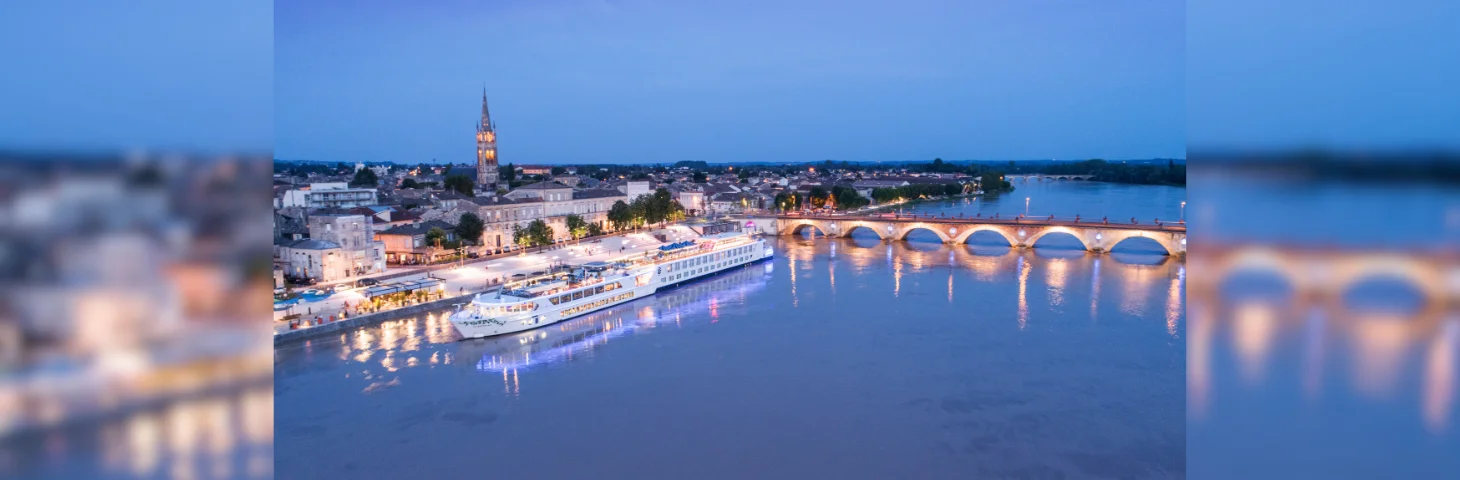 A Uniworld river cruise vessel docked in Libourne, France at dusk.