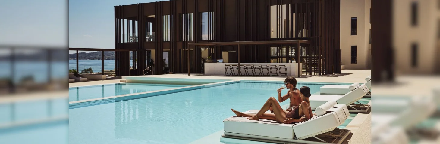 Two people lounging on a poolside lounger at a Domes Resorts hotel.