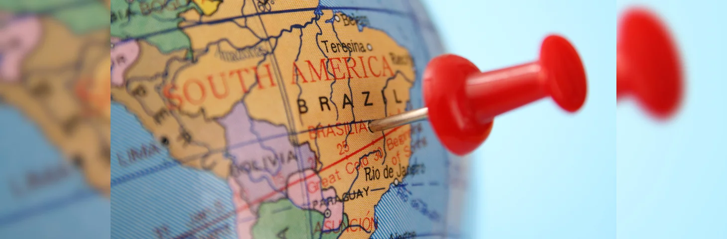 A red pin pushed into Brazil on a world globe.