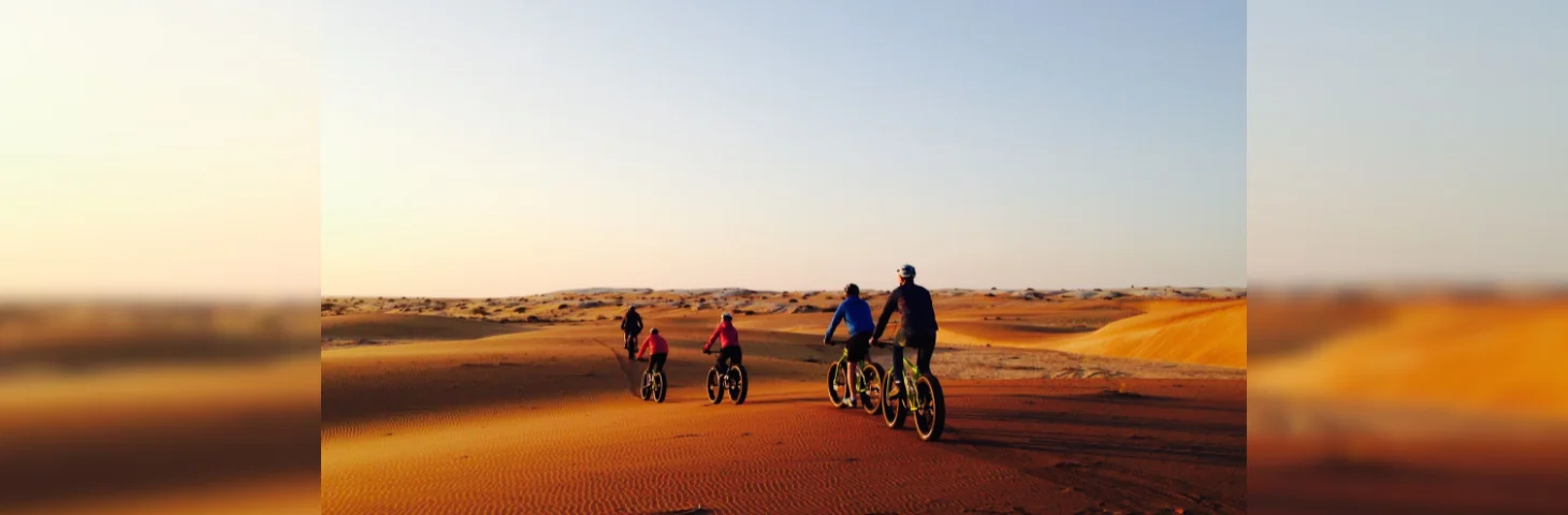 Five people riding bicycles through sand dunes in South Africa near sunset.