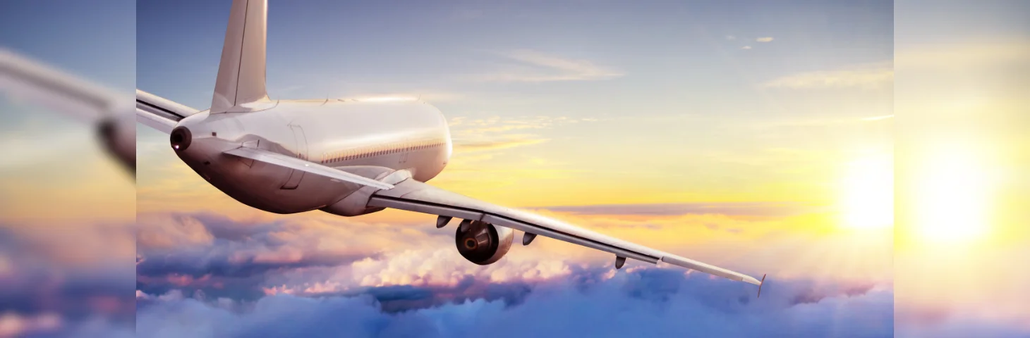 A plane flying over the clouds into the setting sun.