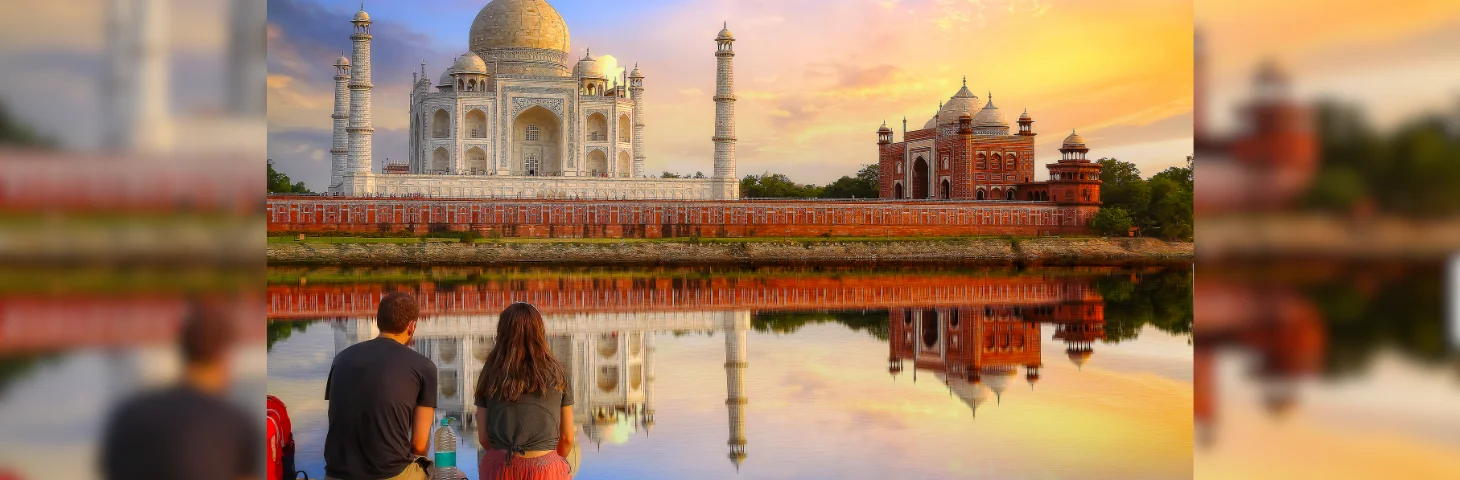 Two people sat over the water from the Taj Mahal in India. 