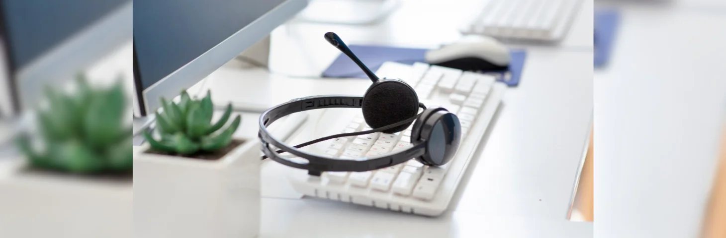 A pair of black call centre headphones laid on top of a white keyboard.