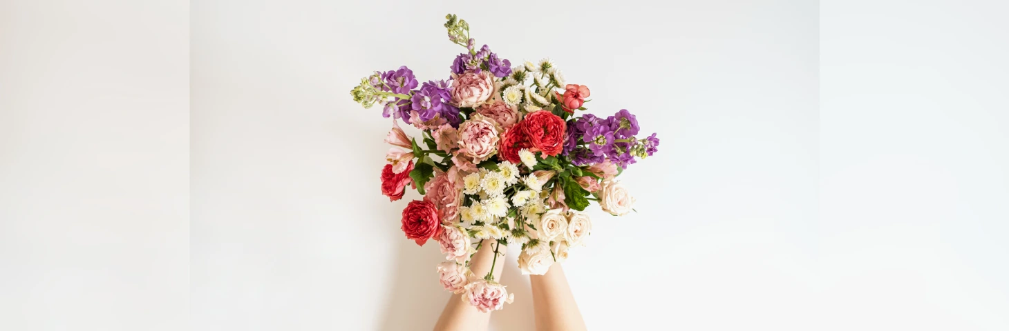 Image of a person holding a bouquet of white, purple, pink and red flowers