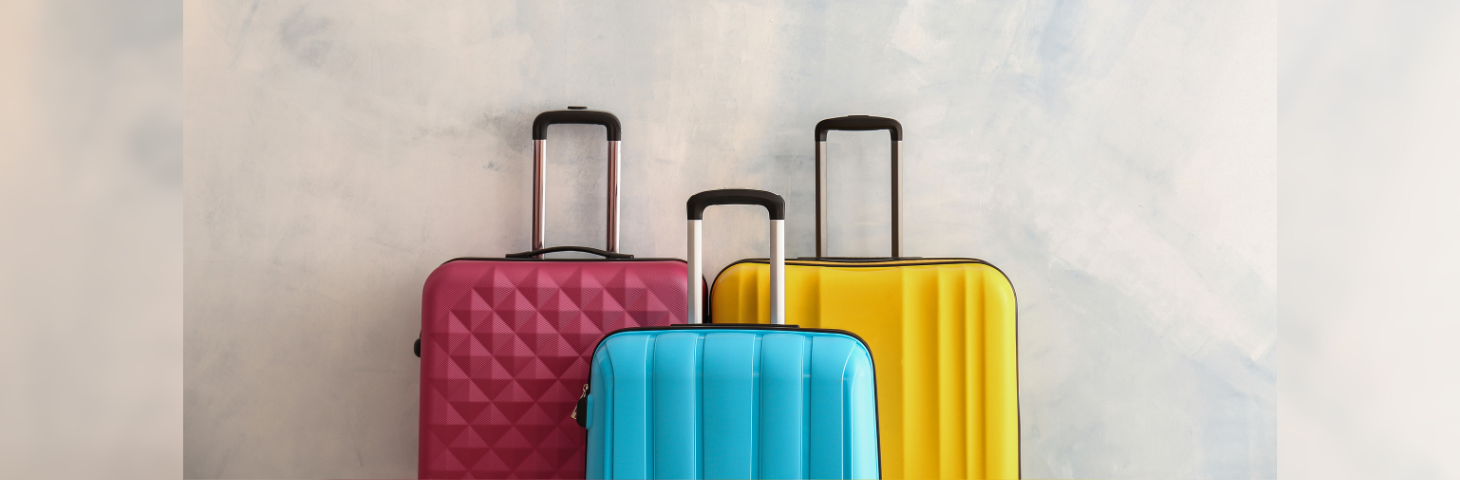 Three suitcases—a pink one, a blue one, and a yellow one, up against a wall.