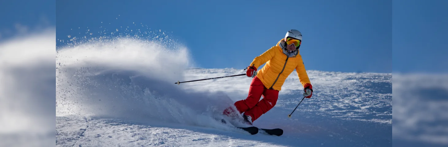 A person in a yellow snowjacket and red trousres skiing.