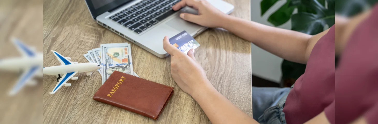 A person holding a credit card up to their laptop whilst booking a holiday.