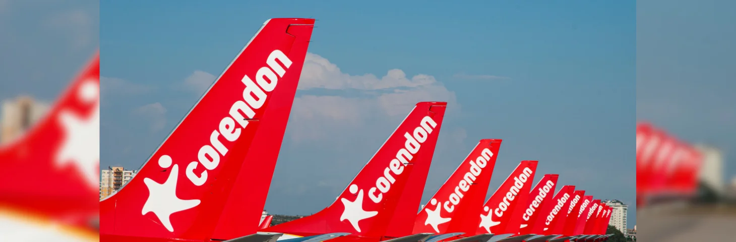 The tails of 12 Corendon Airlines planes, parked at terminals at an airport.