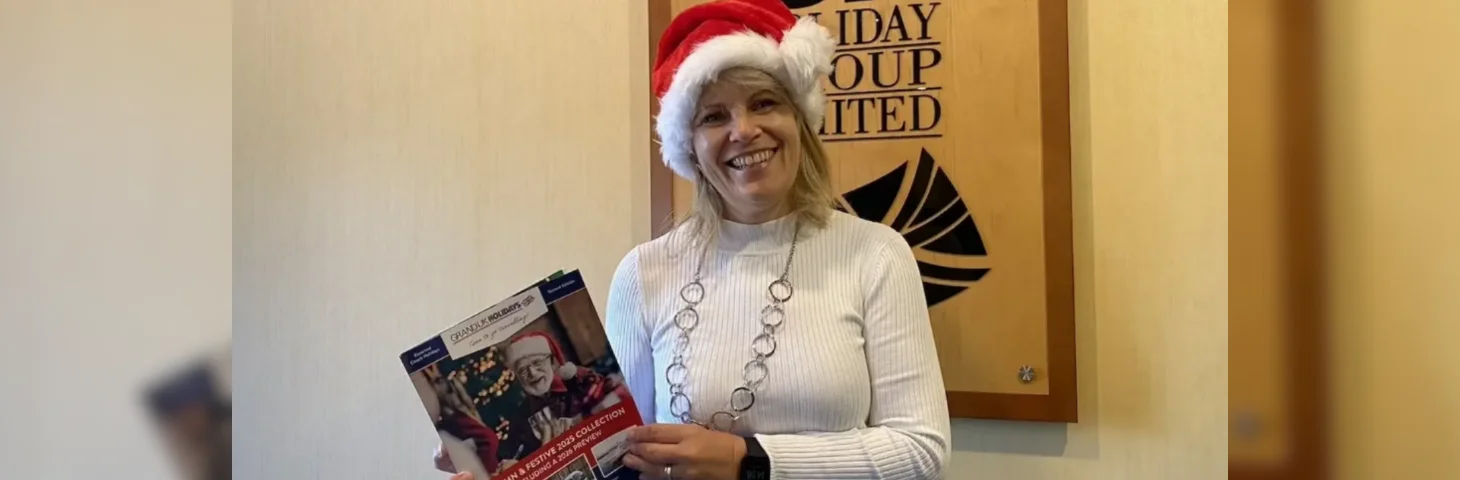 Grand UK Holidays' travel trade manager, Lyn Arnold, wearing a Santa hat and holding a Christmas-themed holiday brochure.