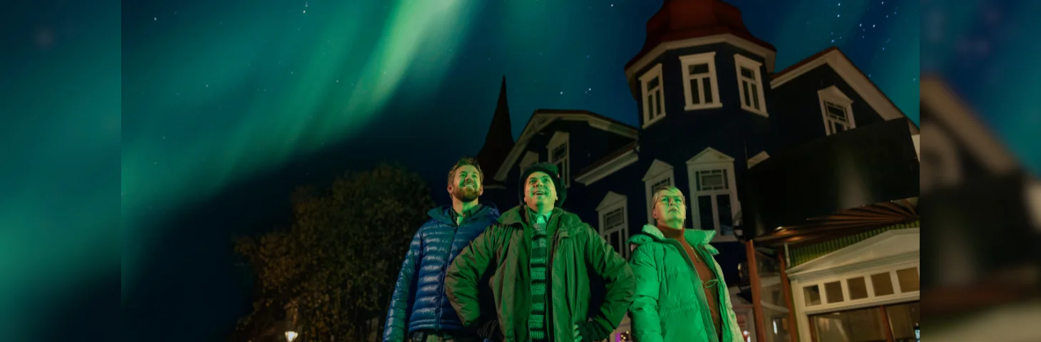 A still from Visit Iceland's A.U.R.O.R.A.S campaign, with star Joe Thomas and other campaign members stood in front of a house under the Northern Lights.