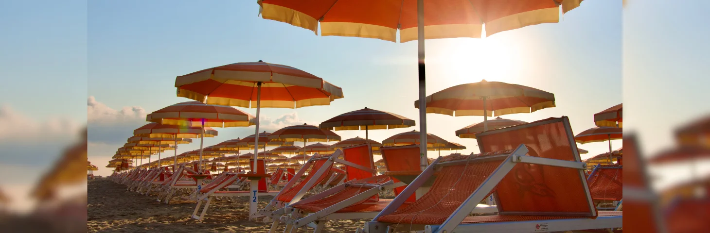 Orange beach umbrellas and deck chairs on a beach.