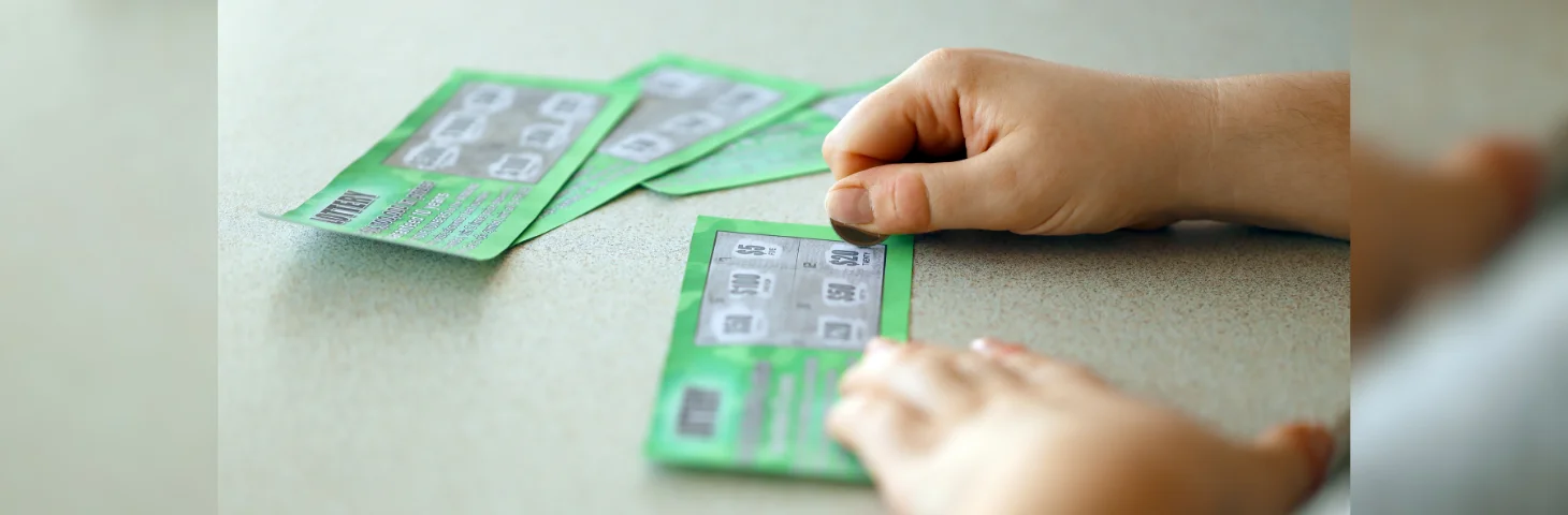 A hand scratching a scratchcard with a small silver coin.