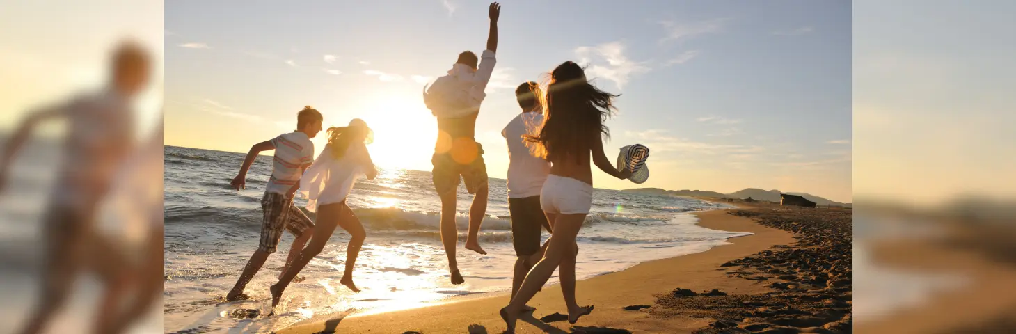Group of friends jumping and running on a beach at sunset
