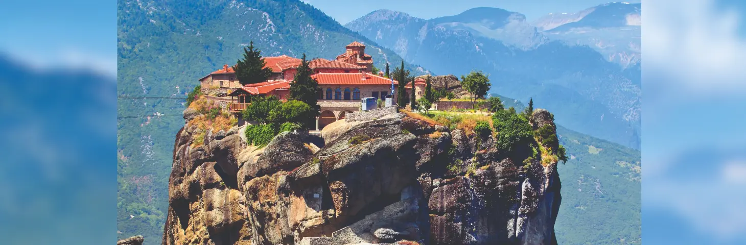 The Meterora Monastery high in the sky on a tall cliff with mountains in the background