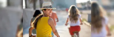 A person in a yellow shirt and hat turning towards the camera, behind them, as they cycle with three fellow holidaymakers.