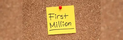 A post it note with 'First Million' written on it in black marker pen pinned to a corkboard.