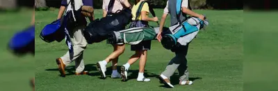 Four golf players carrying their golf bags on the green. 