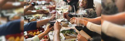 People eating brunch in a restaurant raising glasses of red and white wine to cheers.