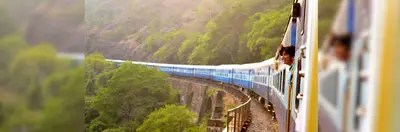 Person looking out of a train window as it winds through green clifftops