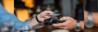 A person wearing a watch holding a card payment terminal to another person.