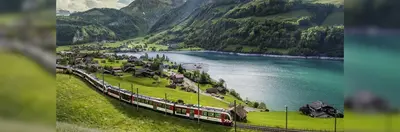 A train traveling along a scenic route next to a lake with mountains in the background. 