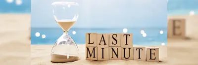 A sand timer on a beach next to wooden alphabet blocks spelling out 'LAST MINUTE'.