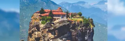 The Meterora Monastery high in the sky on a tall cliff with mountains in the background