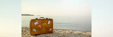 A briefcase covered in travel stickers on a beach