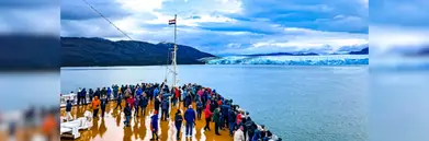 Cruise passengers standing at the front of the ship in front of a glacier