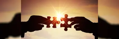 Two puzzle pieces being joined together with a sunset behind.