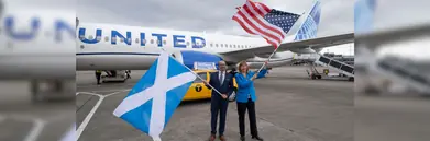 A man and a woman holding a Scottish and a USA flag respectively outside of a United Airlines aircraft