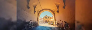 Bikes leaning on wall under archway by sunny town square