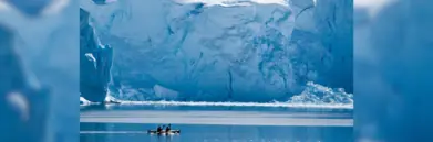 Kayaking on the Polar circle sea with big ice wall behind