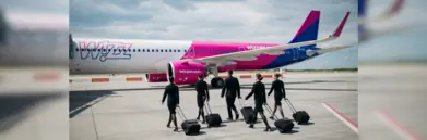 Wizz Air crew walking with suitcases towards a plane on the runway