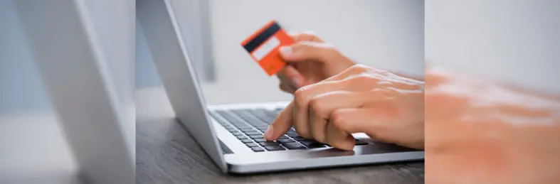 Someone making a payment card on a laptop, reading their card details. 