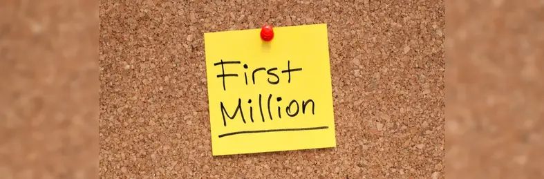 A post it note with 'First Million' written on it in black marker pen pinned to a corkboard.